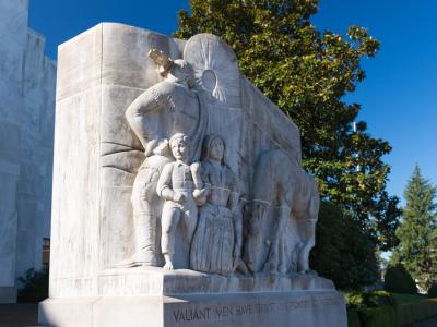 A close-up view of a large white marble bas-relief sculpture depicting pioneers and a covered wagon, with the inscription "VALIANT MEN HAVE THRUST OUR FRONTIERS TO THE SETTING SUN" on the base, situated next to a marble building.
