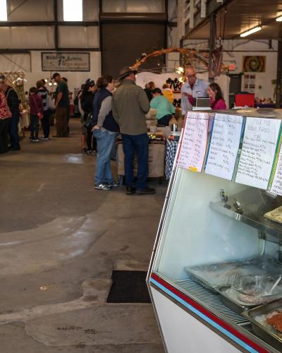 The image shows the interior of a large warehouse-style market with vendors, shoppers, and a seafood display case in the foreground.