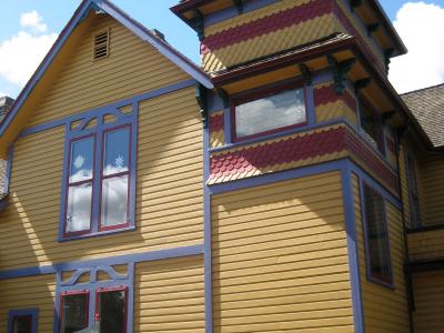 A yellow Victorian-style house with colorful trim, a tower, and a striped awning that reads "THE LATEST SCOOP FOR KIDS AND BABY".